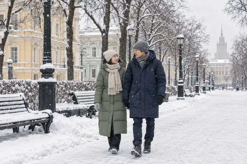 Đôi bạn trẻ người Việt đi dạo trên đại lộ phủ tuyết ở trung tâm Moscow, cô gái mặc áo phao dài màu xanh lá mạ, mũ len và khăn len dày, chàng trai mặc áo parka xanh than dài và mũ len xám, phía sau là hàng cây trụi lá và những dinh thự cổ màu pastel
