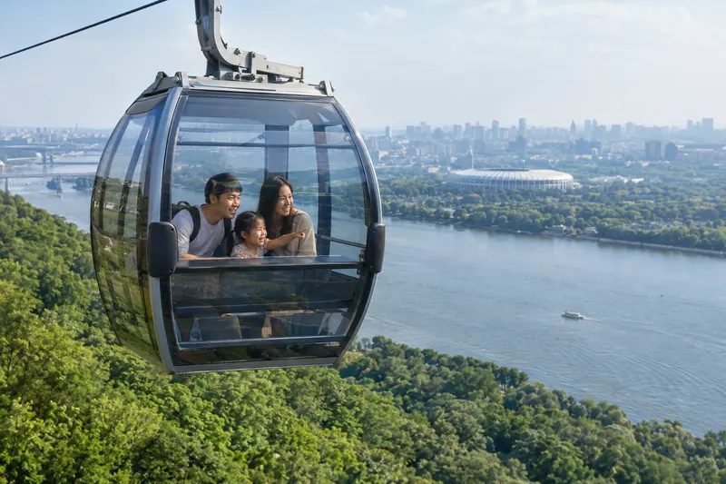 Một gia đình châu Á trong cabin cáp treo bằng kính bay qua sông và đồi cây xanh