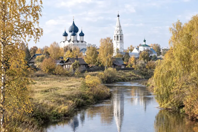 Dòng sông nhỏ uốn qua Suzdal, liễu và bạch dương vàng hai bờ, nhà thờ mái vòm xanh và tháp chuông trắng sau những nếp nhà gỗ
